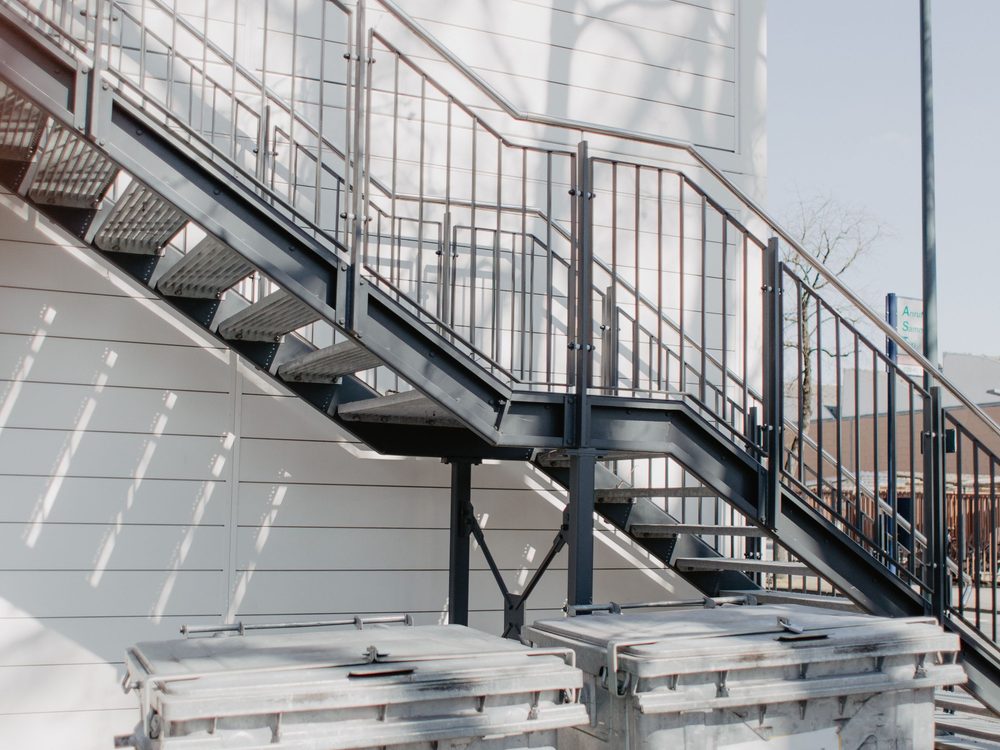 Containers roulants d’une copropriété rangés au pied d’un escalier extérieur
