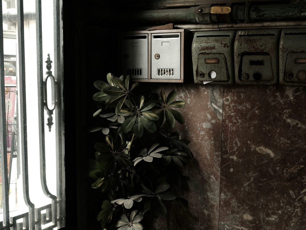 Entrée d’immeuble ancienne avec boîtes aux lettres et sol carrelé, entretien à reprendre